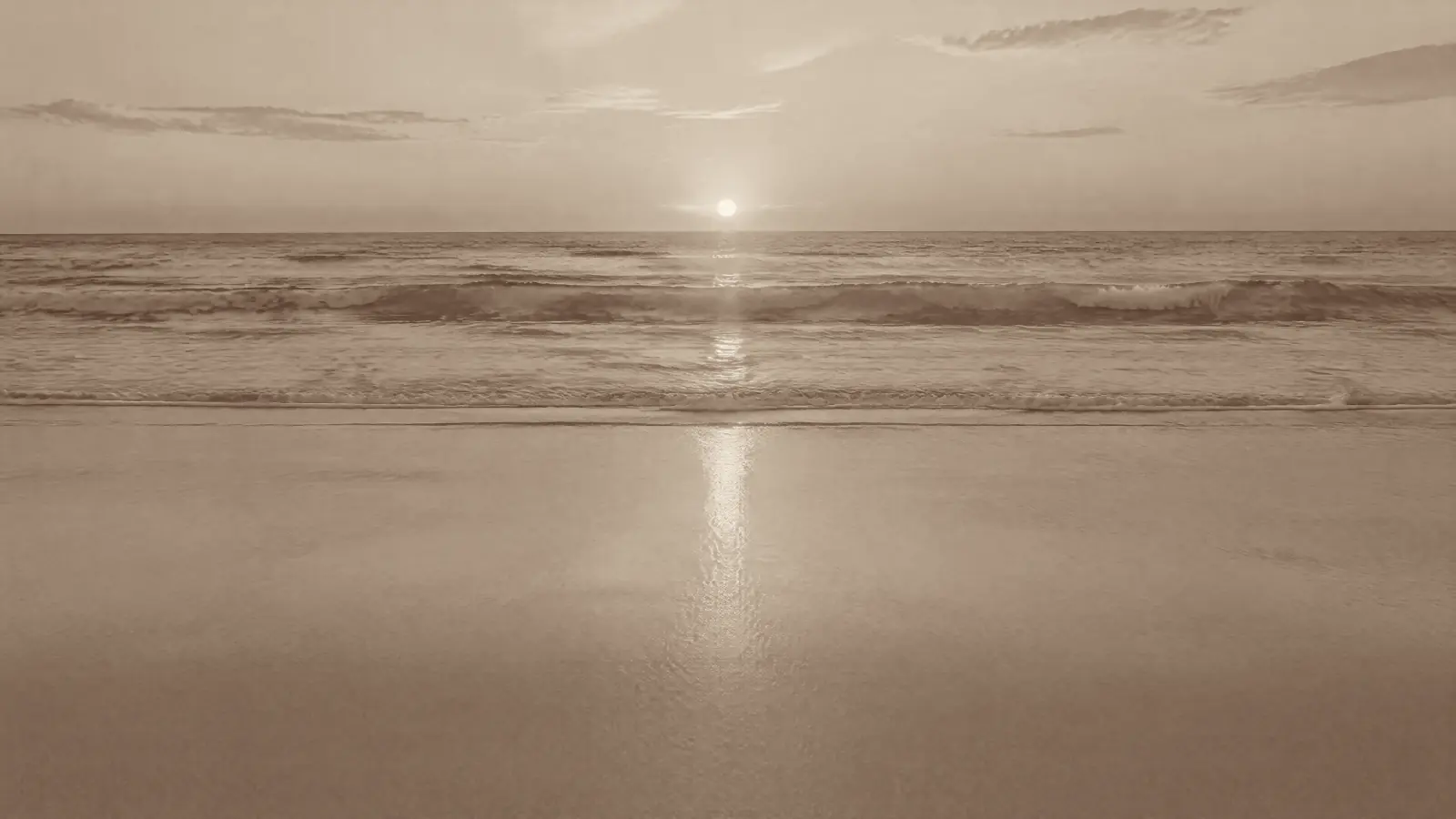 A quiet beach at sunset with turquoise waves and a wide stretch of smooth golden sand